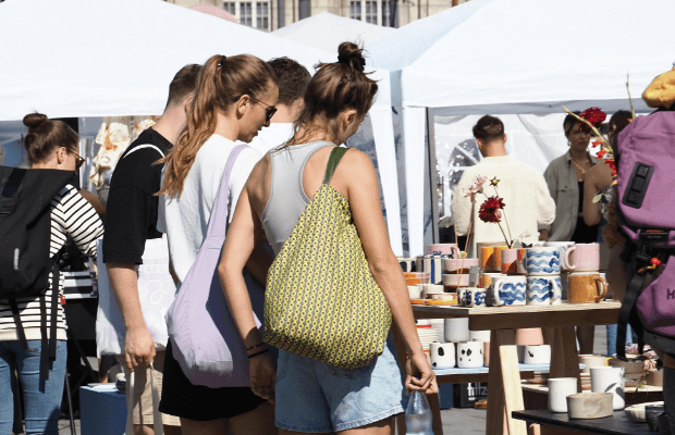 Menschen stehen an einem sonnigen Tag im Freien vor Verkaufsständen und betrachten Keramikware.